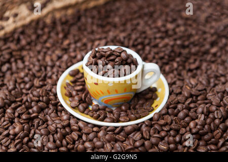 Braun geröstete Kaffeebohnen und eine gelbe Tasse Kaffee mit Bohnen closeup Stockfoto