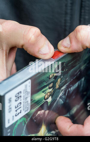 Ladendieb beginnt eine gestohlene DVD Sicherheitsetikett entfernen. Stockfoto