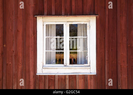 Alte dunkle rote Holzwand mit Fenster in weißer Rahmen, typisch skandinavisch Leben Haus Architektur Detail Stockfoto