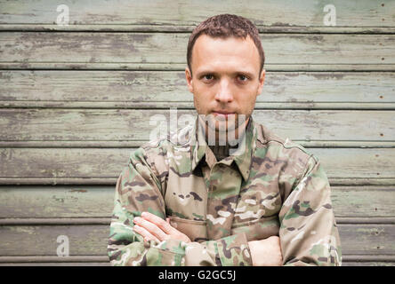 Schönen jungen kaukasischen Mann im militärischen Tarnuniform. Outdoor Closeup Portrait über grüne ländliche Holzwand Stockfoto
