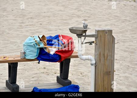 Artikel von Kleidung und persönliche Gegenstände überlassen auf einer Bank als nächstes eine Wasserfontäne am Strand im Assateague island Stockfoto