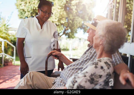 Weibliche nach Hause Bezugsperson, die auf der Suche nach Entspannung auf einer Bank außerhalb ihrer Altenheim älteres Paar. Stockfoto