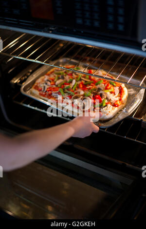 Young Adult Woman, die Pizza im Ofen setzen Stockfoto