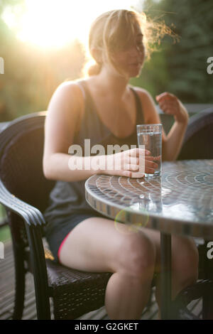 Junge Frau sitzt am Tisch im Freien mit einem Glas Wasser Stockfoto