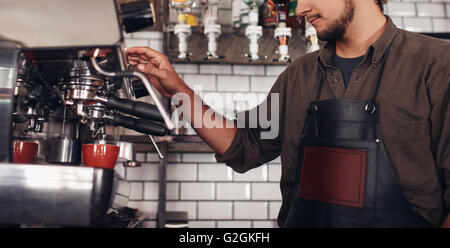 Beschnitten, Schuss von männlichen Barista mit einer Kaffeemaschine, um eine schöne Tasse Kaffee zu machen. Cafe-Arbeiter eine Kaffeezubereitung. Stockfoto