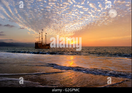 Piraten Schiff Fantasy ist eine alte hölzerne Piratenschiff mit voller Flaggen, wie die Sonne auf dem Ozean untergeht und der Mond in einem bunten s aufgeht Stockfoto