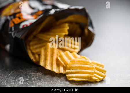 Runzeln Sie geschnittene Kartoffelchips auf alten Küchentisch. Kartoffel-Chips aus Verpackung ausgegossen. Stockfoto