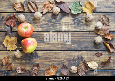 Herbstlaub, Äpfeln und Nüssen auf Holz Hintergrund Stockfoto