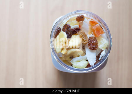 Kunststoff-Glas mit gemischte Trockenfrüchte über Holzoberfläche. Selektiven Fokus. Erhöhte Ansicht Stockfoto