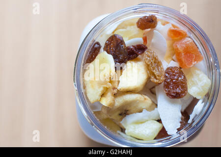 Kunststoff-Glas mit gemischte Trockenfrüchte über Holzoberfläche. Selektiven Fokus. Erhöhte Ansicht Stockfoto