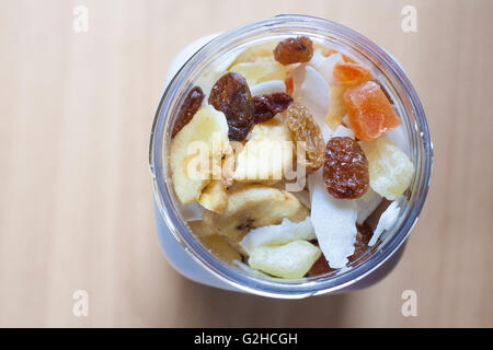 Kunststoff-Glas mit gemischte Trockenfrüchte über Holzoberfläche. Selektiven Fokus. Erhöhte Ansicht Stockfoto