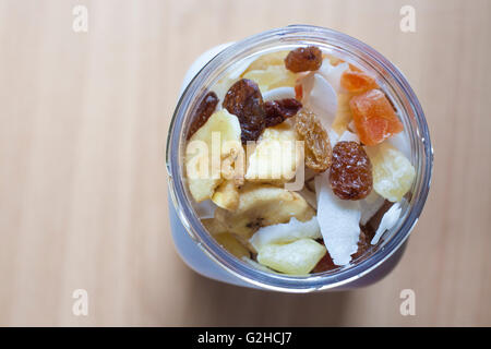 Kunststoff-Glas mit gemischte Trockenfrüchte über Holzoberfläche. Selektiven Fokus. Erhöhte Ansicht Stockfoto