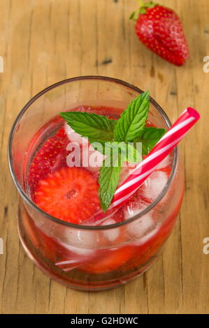 Erdbeersaft in einem krummen Trinkglas auf einem Holztisch Stockfoto