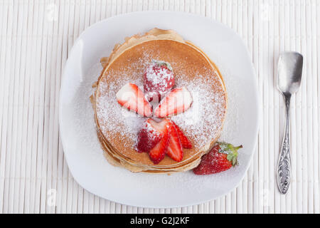 Pfannkuchen auf weißem Hintergrund mit Erdbeeren und Zucker und silbernen Löffel Stockfoto