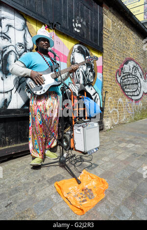 Eine Straße Straßenmusiker spielt Geld mit einer e-Gitarre für Spenden auf der Brick Lane in London während der 1. Mai Feiertag Stockfoto