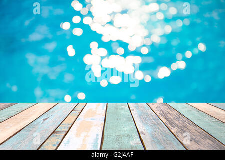 Perspektive Holz Tischplatte und Soft Fokus Bokeh Lichteffekte über eine wellige, blaues Wasser Hintergrund in den Pool, Warenpräsentation Stockfoto