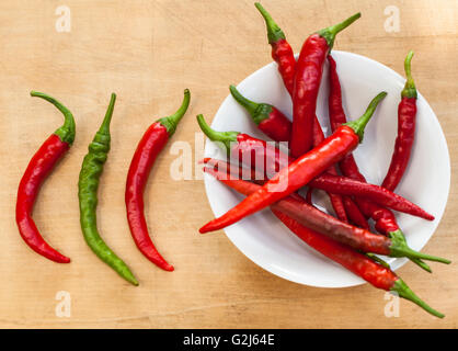2 Chilischoten rote und eine grüne neben einer Schüssel voll mit roten chilis Stockfoto