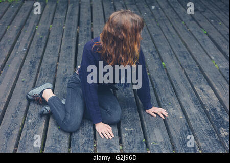 Eine junge Frau sitzt auf einer großen Holzterrasse Stockfoto