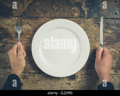 Overhead Schuss von Händen mit Messer und Gabel von einem weißen Teller auf einem Holztisch Stockfoto