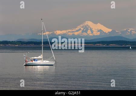 Ein Segelboot aus Weiden Strand in Oak Bay in Victoria, British Columbia.  Im Hintergrund ist Mt. Baker in Washington State, USA. Stockfoto