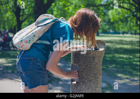 Eine junge Frau trinkt aus einem Brunnen in einem Park an einem sonnigen Tag im Sommer Stockfoto