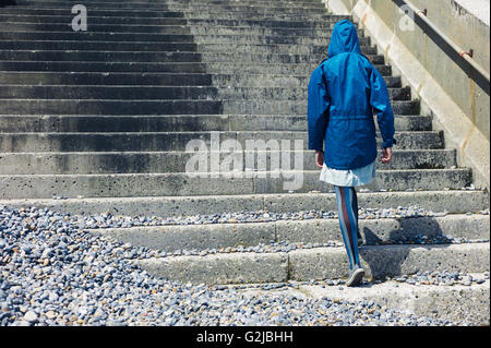 Ein junger Mensch trägt eine blaue wasserdichte Jacke ist ein paar Stufen außerhalb an der Küste Wandern. Stockfoto