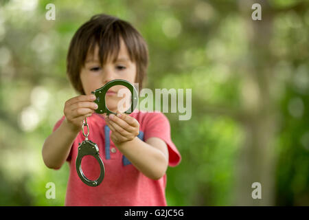 Niedliche kleine Junge mit Handschellen an den Händen, spielen Stockfoto