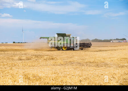 John Deere Mähdrescher erntet Weizen in Oklahoma, USA. Windkraftanlagen sind im Hintergrund. Stockfoto