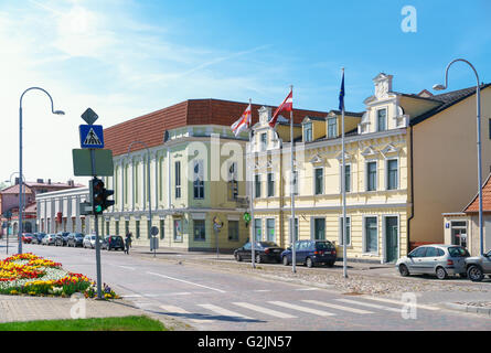 Ventspils, Lettland - 8. Mai 2016: Alten gelben Gebäude mit Flaggen in Ventspils in Lettland. Es ist eine Stadt in der Region von Courland Lettlands. Lettland gehört zu den baltischen Staaten. Menschen auf der Straße Stockfoto