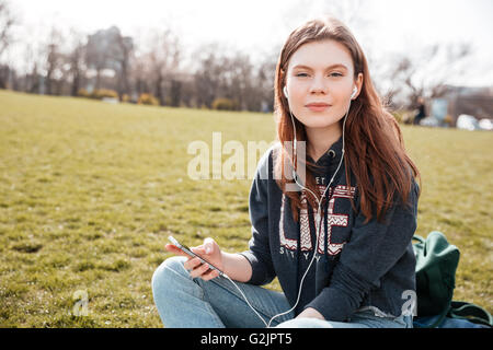 Ziemlich ruhige junge Frau anhören von Musik vom Mobiltelefon auf dem Rasen Stockfoto