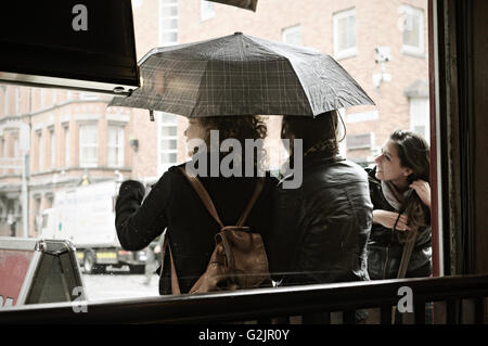 Junge Frauen mit einem Regenschirm während einer Dusche aus gesehen, in einem Restaurant in Dublin, Temple Bar Viertel, Irland Stockfoto