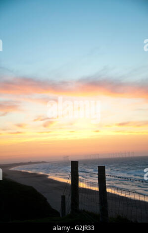 Post & Draht Zaun Silhouette auf Klippe Windkraftanlagen in Redcar Beach produzieren erneuerbare Bioenergie im Meer bei Sonnenuntergang Stockfoto