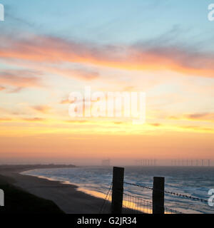 Post & Draht Zaun Silhouette auf Klippe Windkraftanlagen in Redcar Beach produzieren erneuerbare Bioenergie im Meer bei Sonnenuntergang Stockfoto