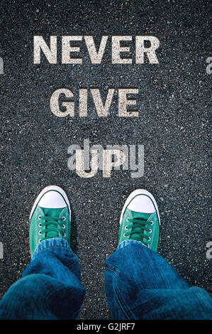 Neue grüne Schuhe von oben auf Asphalt mit Zeichen niemals aufgeben Stockfoto