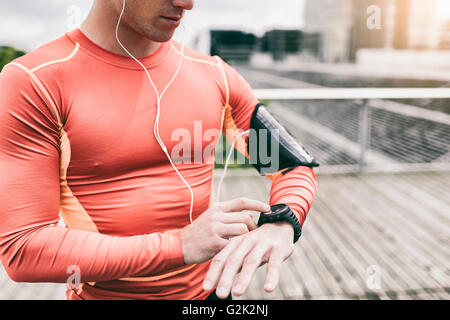 Urban Runner-Mann sucht app auf Sportwatch. Männchen laufen Joggen Smartwatch außerhalb Stockfoto