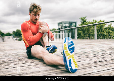 Städtischen sportlichen Mann stretching außerhalb auf Holzbrücke Stockfoto