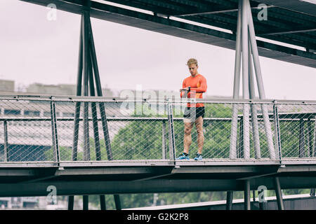 Mann sucht Sportwatch ausgeführt. Männliche Läufer Joggen mit Smartwatch auf Metallbrücke Stockfoto