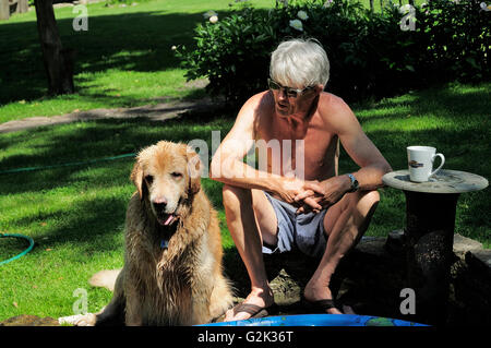 Ältere Mann sitzt im Hinterhof mit seinem englischen Golden Retriever Watson. Stockfoto
