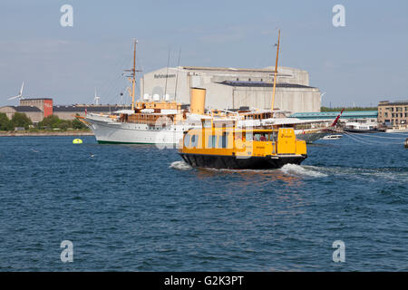 Eine gelbe Hafen Bus vorbei die verankerte dänische Königliche Yacht HDMY Dannebrog auf Holmen in den Hafen von Kopenhagen. Stockfoto