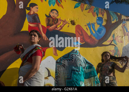 Drei weibliche Pilger vor Wand gemalt mit Krishna das Flötenspiel bei Shipra Fluß Ghats, Shahi Snaan (Royal Stockfoto