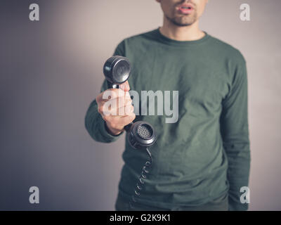 Ein besorgt und beunruhigt aussehender junger Mann hält den Empfänger eine Vintage Telefon mit Wählscheibe Stockfoto