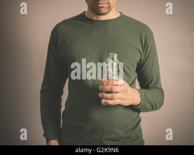Ein junger Mann trägt einen grünen Top hält eine kleine Glasflasche Stockfoto