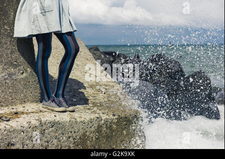 Die Beine einer jungen Frau trägt ein Kleid wie sie steht auf einem Felsen an der Küste mit den Wellen, die in Stockfoto