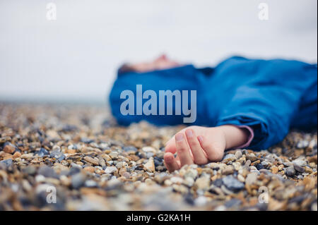 Eine unbewusste Frau liegt auf einem Kiesstrand Stockfoto