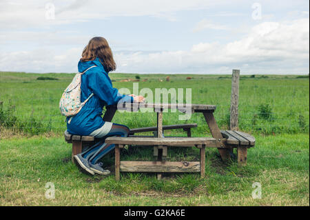 Eine junge Frau sitzt einen Picknicktisch draußen in einem Feld Stockfoto