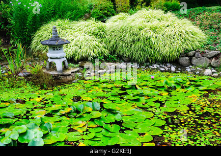 Eine japanische Laterne sitzt neben einem Seerosenteich im japanischen Garten auf Mayne Island, British Columbia. Stockfoto