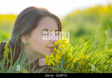 Porträt von schöne junge langhaarige Frau im Park liegen und die Blumen riechen Stockfoto