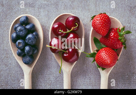 Heidelbeeren, Kirschen und Erdbeeren auf Holzlöffel am Steintisch, Ansicht von oben Stockfoto