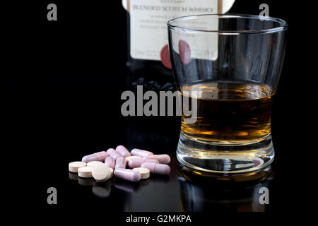 Wiskey in ein Glas einige Pillen und die Flasche hinter auf schwarzem Hintergrund Stockfoto