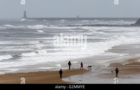 Am ersten Sommertag machen die Menschen einen nassen und windigen Spaziergang am Tynemouth Beach in Tyne & Wear. Stockfoto